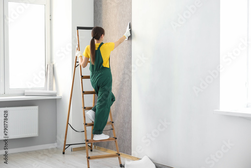 Woman smoothing stylish gray wallpaper in room photo