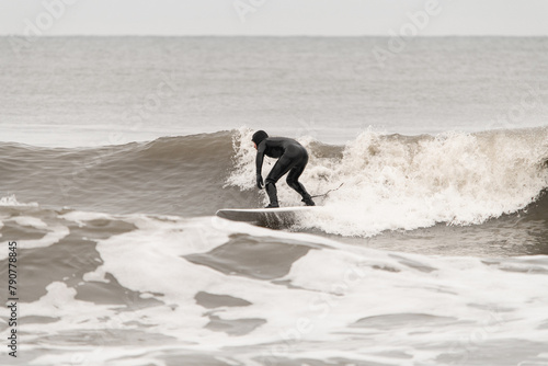 Male surfer in a black wetsuit stands confidently on a surfboard, riding a wave