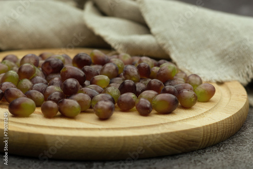 Grapes on a wooden round cutting board. Grapes on a background of burlap. Fruit close-up. Scattered grapes.