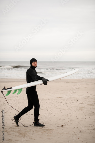 Male surfer walks along the sandy seashore with his surfboard in his hands