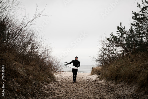 Happy male surfer walks away from the sea on a sandy path