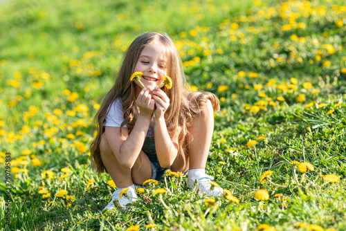 Portrait of little cute girl sitting with dandelions on the grass. Happy smiling girl lies on the grass among yellow flowering dandelions in the park. Spring concept. Happy life without allergy.