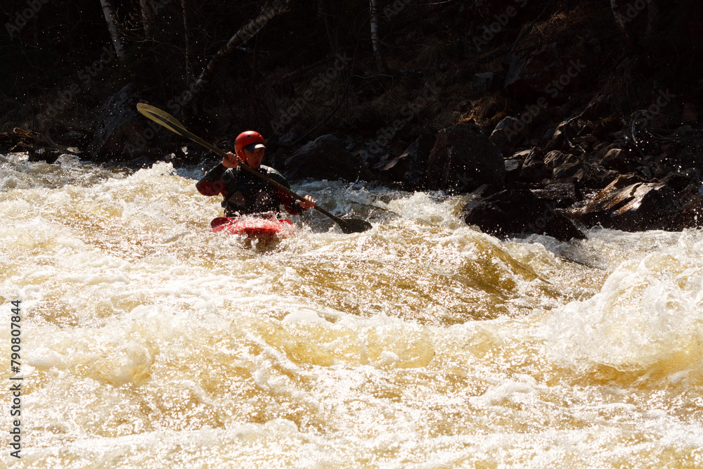 A man in a red kayak is paddling through a river