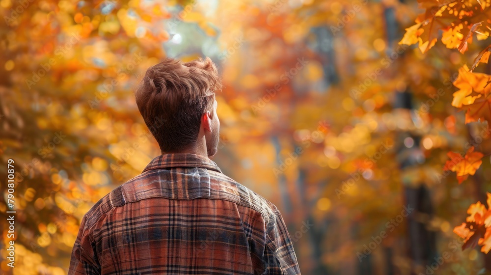 Young man enjoys the beauty of the autumn forest, standing with his back to the viewer Young man enjoys the beauty of the autumn forest, standing with his back to the viewer