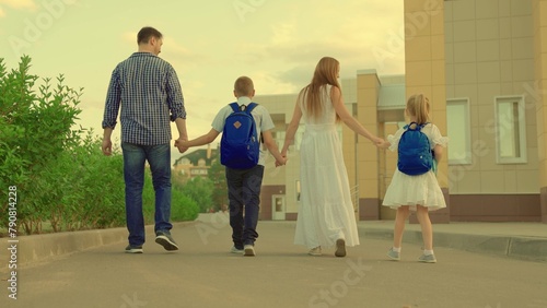 Happy family, son, daughter, dad, mom go to school together with children. Concept of childrens school education. Family walks holding hands along city street. Happy kids, parents on weekend walk photo