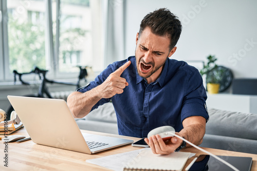 Furious angry man screaming at smart speaker while working from home