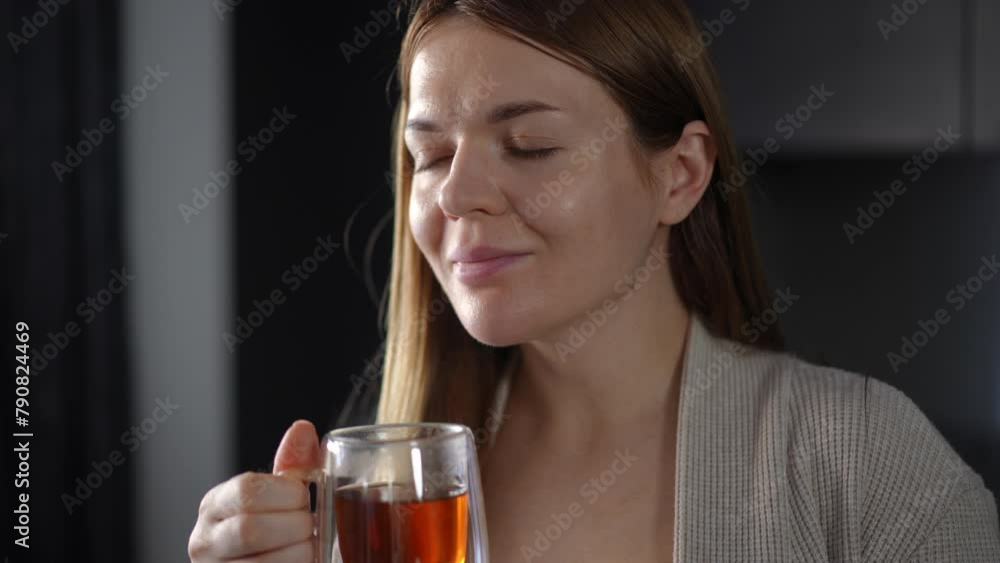 Close-up. Happy woman enjoying the aroma of freshly brewed tea in a glass cup in her hand. The woman inhales the aroma of tea and closing eyes, smiles Close-up. Happy woman enjoying the aroma of freshly brewed tea in a glass cup in her hand. The woman inhales the aroma of tea and closing eyes, smiles