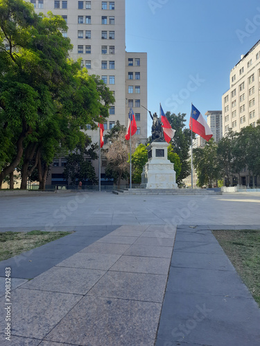 Centro da cidade de Santiago Chile com poucas pessoas e em manhã ensolarada, mostrando a arquitetura do local. Plaza de La Ciudadania com bandeiras do Chile.