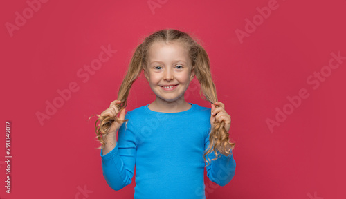 Little cheerful girl plays with her hair on a pink background.