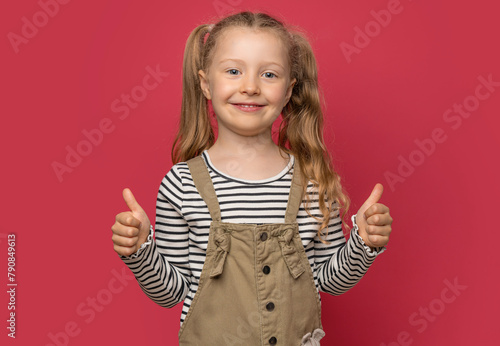 Little cheerful girl shows thumbs up on a pink background.