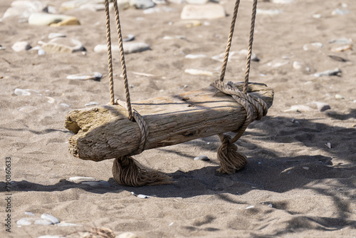 A swing standing on the sea sand. Oceanside swing made from driftwood sea logs. Vintage swing standing in the sand on the seashore.