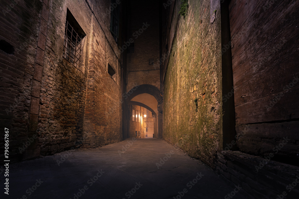 Fototapeta premium Dark narrow empty medieval street in historical center of European town, Siena, Italy