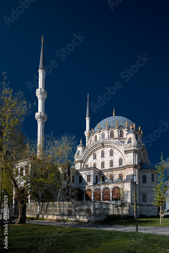 Ancient Nusretiye Mosque surrounded by trees against dark blue sky on sunny day, Istanbul, Turkey photo