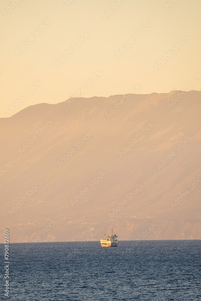 A cruise ship sailing in the sea against mountain during sunrise in the place called Drosia in ths island of zakynthos in Greece