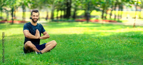 Portrait of brunette bearded man coach practicing yoga, sit in half lotus exercise, ardha padmasana pose, wile meditation session in park. Wide horizontal banner image with copy space area photo