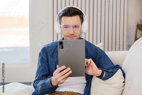 Focused man with headphones uses a tablet, immersed in digital interaction, in a comfortable home environment.