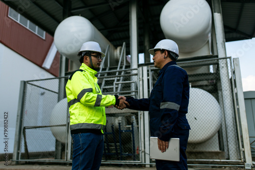 Two men in safety gear shake hands. One of them is holding a tablet. Scene is professional and friendly