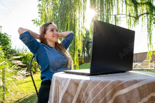Mujer trabajando feliz con su laptop al aire libre, en el jardín de su casa photo
