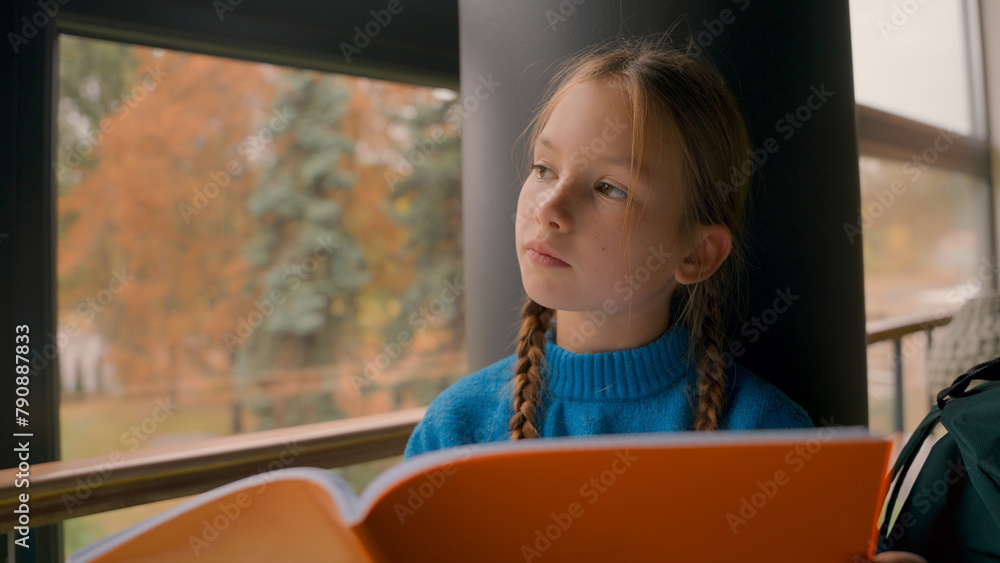 Little red-haired European girl sitting reading notebook studying school homework knowledge looking window pupil prepare lesson schoolgirl education learn task exam cognition notes gymnasium indoors - obrazy, fototapety, plakaty 