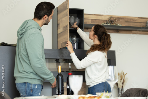 couple taking out the glasses from the cabinet to set the table on a special day photo