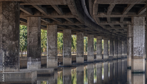 Perspective view of concrete pillars under Khlong Toei Expressway, with calm surface water reflection wonderful shadow, shape, lines and curve the underside support beams of the road along the canal.