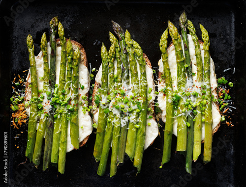 Grilled asparagus toast with cheese and herbs on a black background, top view. Delicious vegetarian toasted sandwich