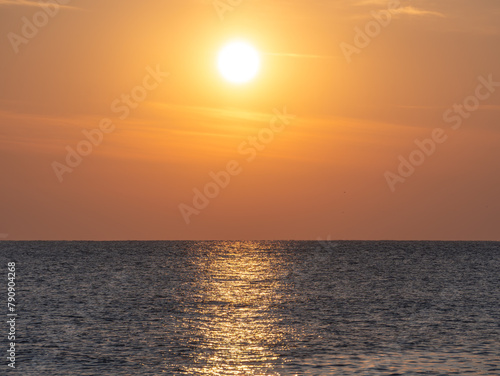 Fototapeta Naklejka Na Ścianę i Meble -  The sun sets over a calm ocean, with golden light reflected on the water