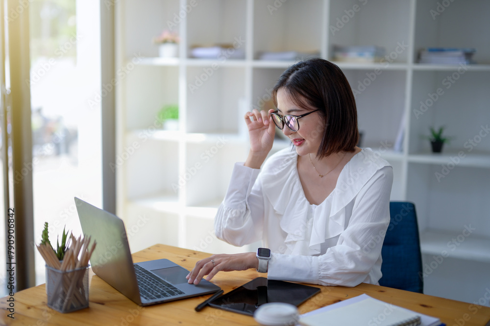 Focused businesswoman with glasses analyzing data on her laptop at office workspace. Focused businesswoman with glasses analyzing data on her laptop at office workspace.