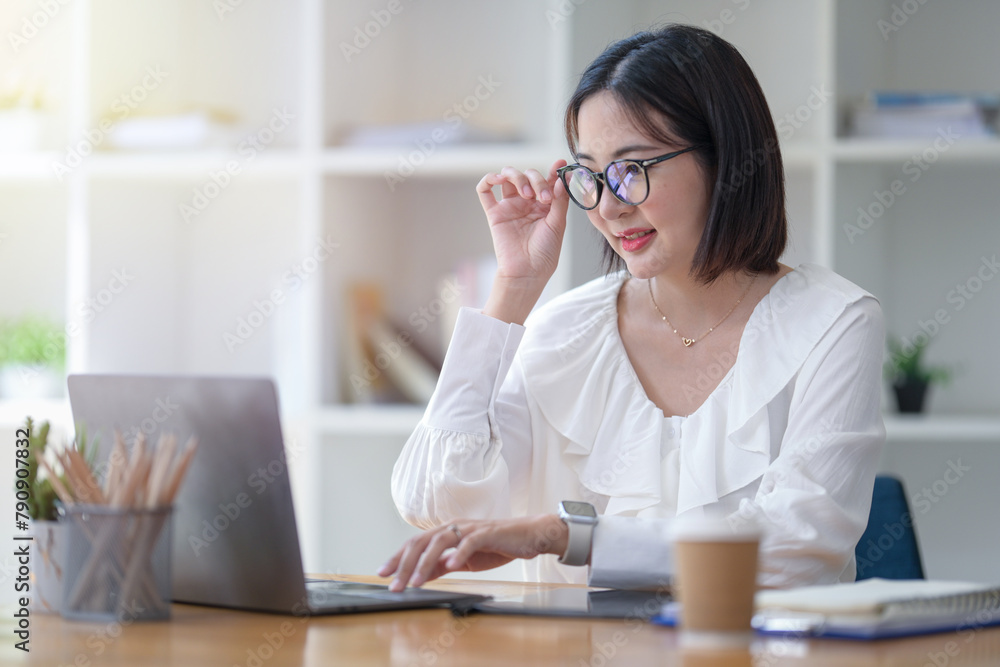 Focused businesswoman with glasses analyzing data on her laptop at office workspace. Focused businesswoman with glasses analyzing data on her laptop at office workspace.