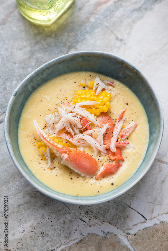 Bowl of corn soup served with crab meat, vertical shot on a light-grey granite surface, elevated view