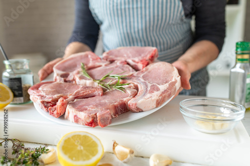 Fresh and raw pork chops on a plate holding by woman hands in the kitchen. Preparing food