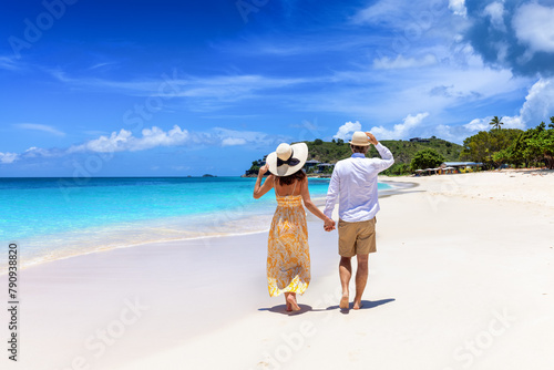 Happy holiday couple with sunhats walks down a tropical beach with turquoise sea in the Caribbean, Antigua island