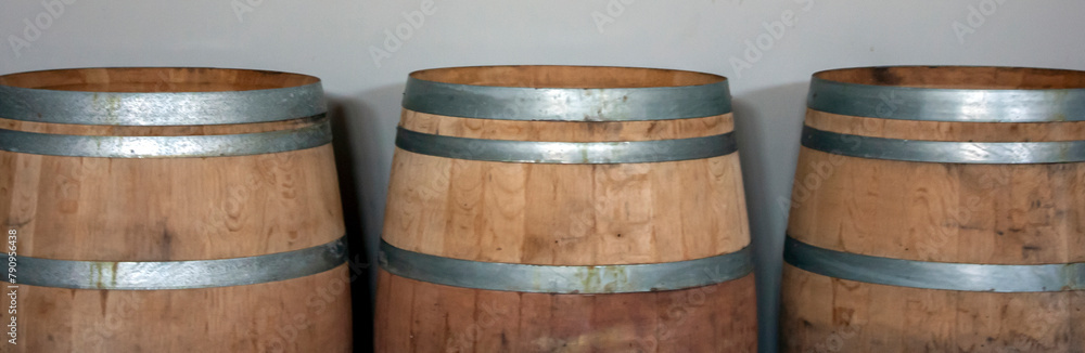 Three oak barrels stand against the wall. Wooden barrels are tied with steel hoops. Metal and natural wood of wine barrels Three oak barrels stand against the wall. Wooden barrels are tied with steel hoops. Metal and natural wood of wine barrels