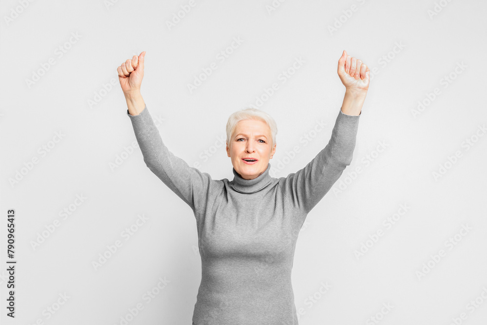 Joyful senior lady with arms raised on grey background