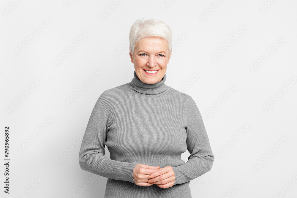 Senior woman with hands clasped, smiling on grey background Senior woman with hands clasped, smiling on grey background