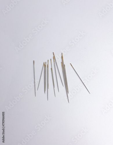 A bunch of tailoring cloth sewing thin stainless steel needles with gold colored top hole. Small object photography isolated on vertical ratio background.
