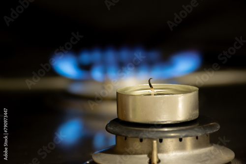 Gas burner beneath candle creates electric blue flame in darkness