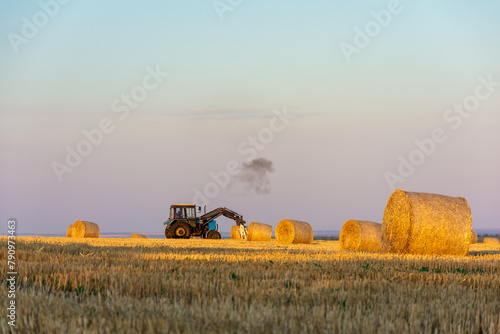 Tractor in grassy field with hay bales under cloudy sky