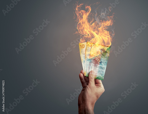 Obraz na płótnie Hand holding burning Swiss franc banknotes showing concept of inflation or money