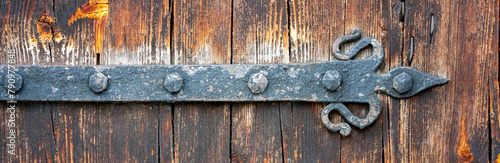 Rusty old door hinge close-up. Forged hinge on an old wooden door. A weather-beaten door made from weathered old boards.