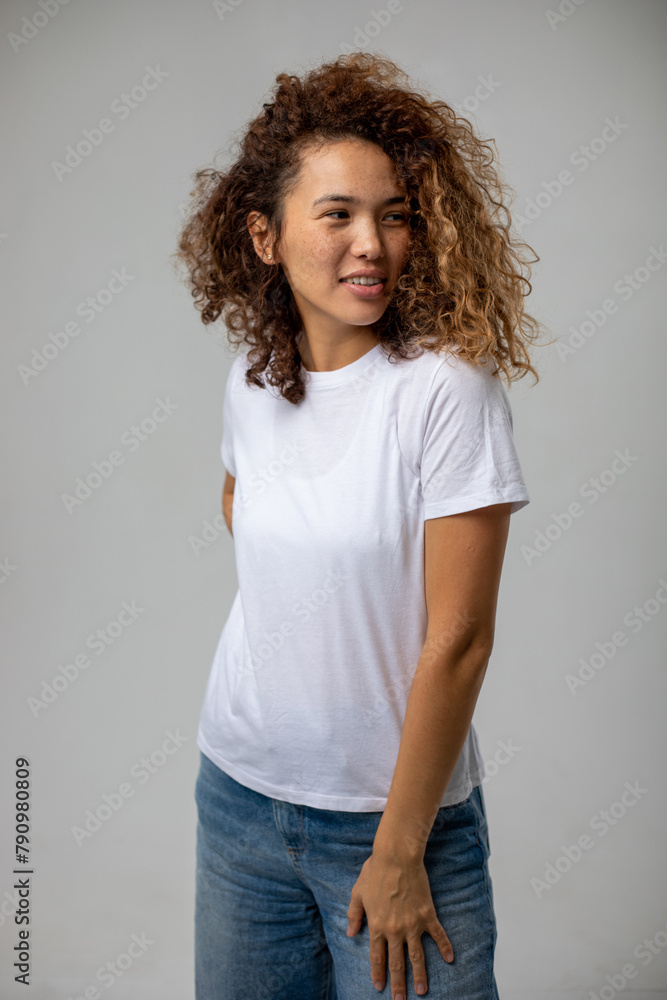 T-shirt design and advertising concept. Style and fashion. Indoor shot of cheerful smiling young African American woman with curly hair pointing index finger at copy space on her blank white top T-shirt design and advertising concept. Style and fashion. Indoor shot of cheerful smiling young African American woman with curly hair pointing index finger at copy space on her blank white top