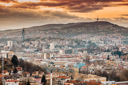 panorama of Sarajevo as the sun sets behind its rolling hills, casting a colorful hue over the cityscape.