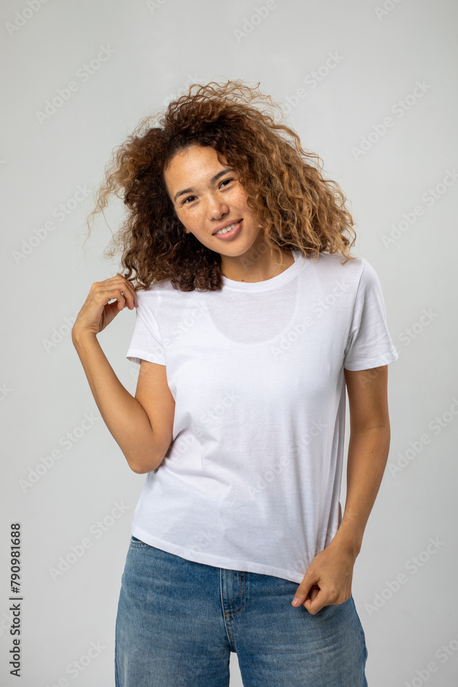 T-shirt design and advertising concept. Style and fashion. Indoor shot of cheerful smiling young African American woman with curly hair pointing index finger at copy space on her blank white top T-shirt design and advertising concept. Style and fashion. Indoor shot of cheerful smiling young African American woman with curly hair pointing index finger at copy space on her blank white top