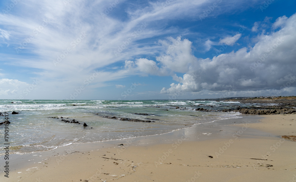 Une plage de sable entrecoupée de sillons rocheux, des eaux transparentes reflétant le vert à l'horizon, sous un ciel bleu parsemé de nuages blancs, en Bretagne. Une plage de sable entrecoupée de sillons rocheux, des eaux transparentes reflétant le vert à l'horizon, sous un ciel bleu parsemé de nuages blancs, en Bretagne.