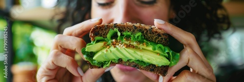 Girl bites off an avocado sandwich made from black bread photo