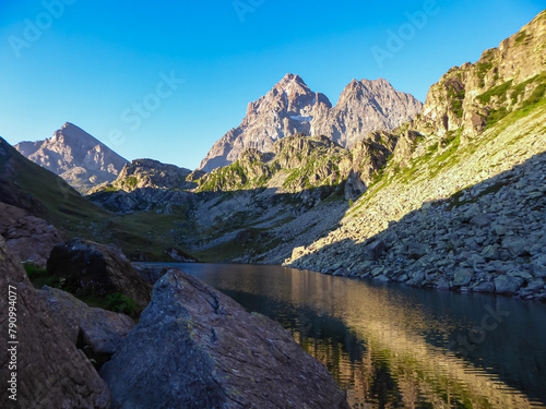 Scenic sunrise view of mountain summit Monte Viso (Monviso) and lake Lago Grande di Viso in the Cottian Alps, Piemonte, Italy, Europe. Rock walls of Stone king are shining in warm red orange colors