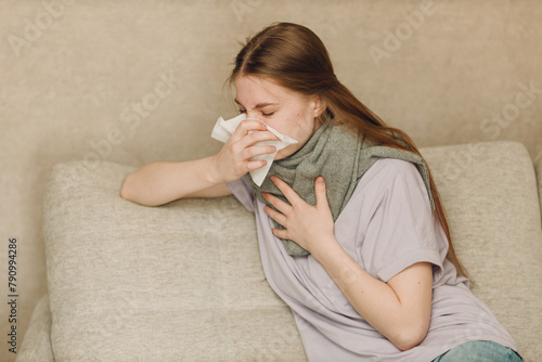 Young woman wearing scarf has flu ill sick disease cold at home indoor on sofa with napkins