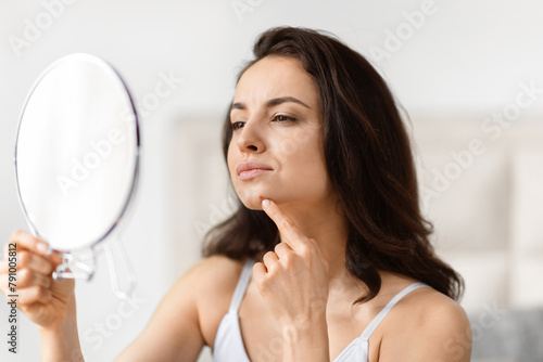 Young woman is closely inspecting her facial skin in bathroom