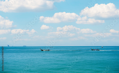 Fisherman riding traditional long tail fishing boats in sea with rock mountain against blue sky with cloud at Ao Nang Beach - Krabi, Thailand. © surasak