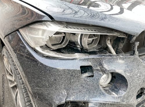 The front part and the headlight of the black car were damaged as a result of a traffic accident. The front part of the car, damaged and broken as a result of an accident. Hood, headlight, bumper. 